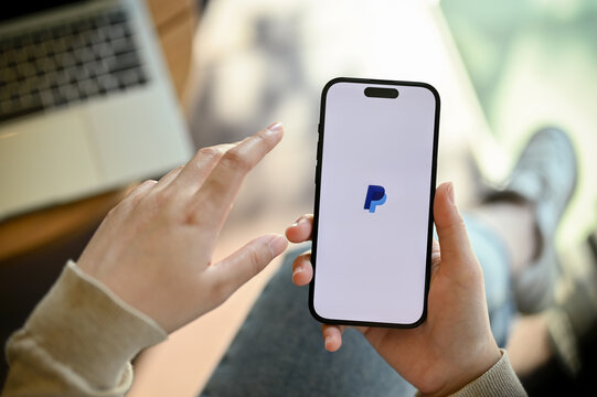 Close-up image of a woman's hand holding a smartphone with PayPal logo on screen