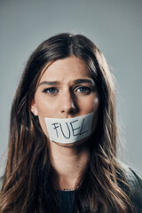 Woman, face and tape on mouth for fuel prices, ecumenic struggle or financial crisis against gray studio background. Portrait of female activist with covered lips in silence, speech or voice message - obrazy, fototapety, plakaty
