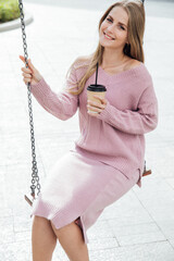 fashionable woman with a cup rides on a swing