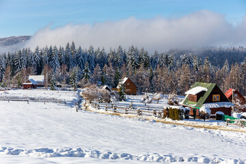 Plone farm village in Zabnica, Wegierska Gorka, Poland, traditional wooden mountain style cottages covered with snow with snowy Beskid Mountains and meadows around.