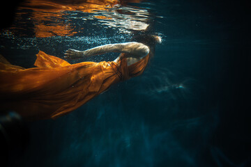 Young beautifull caucasian woman in orange dress under water
