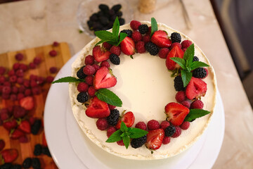 process of making homemade White cream cake decorated with berries and green mint leaves
