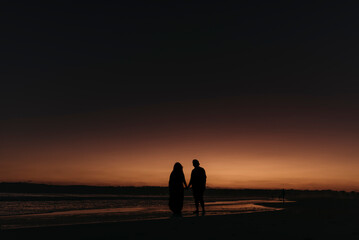 Silhouette of husband and wife walking on beach at sunset