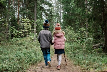 brother and sister holding hands walking through the forest in fall