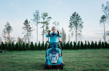 boy cutting grass with mower in the garden in summer