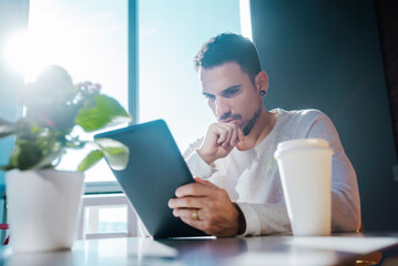 Stylish young man sitting on couch in a cafe using tablet