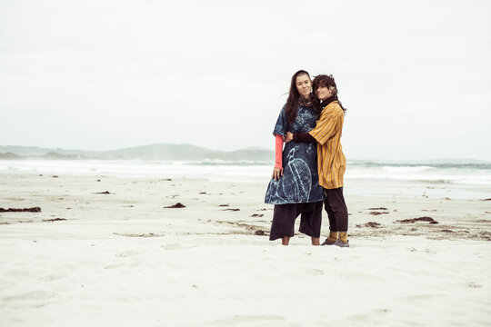 Same sex lesbian couple hug on wild remote beach adventure in the wind