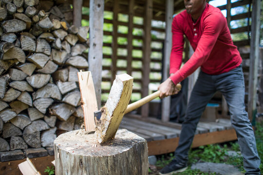 Strong Indian man splitting firewood with sharp axe.