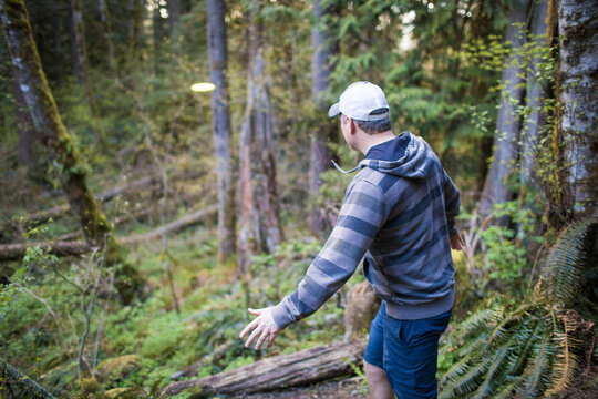 Man throws frisbee in forest during a disk golf game.