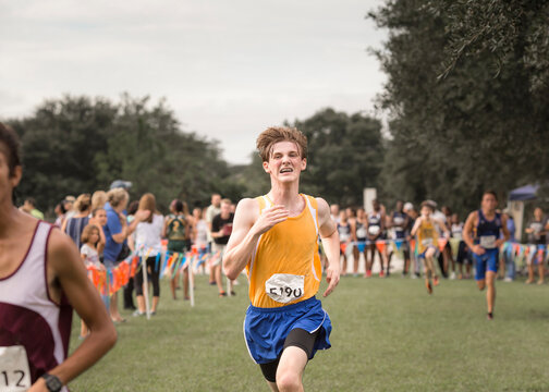 Teen male cross country runner with braces crosses finish line in race