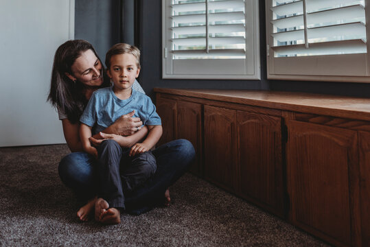 Smiling mom sitting on floor with 5 yr old son on lap near window