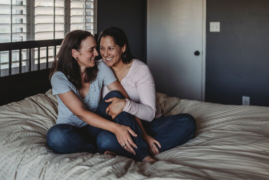 Happy Same Sex Couple Sitting On Bed Laughing Together