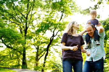 Dad holding son on shoulders in park with mom looking up