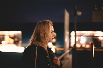 Young woman standing at subway station by moving train at night