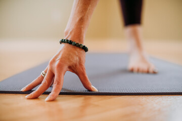 Close up female hand with bracelet and bare foot on yoga mat in studio