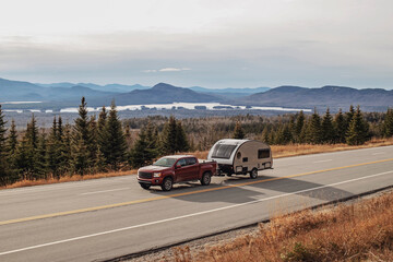 Pickup truck and RV camper drive along scenic road in Jackman, Maine