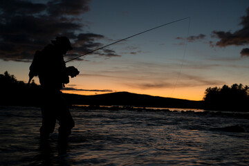 A lone fly fisherman tying on a fly at sunset in Maine.