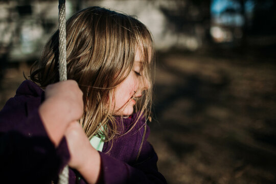 Young Girl's Face In Winter Sunlight On Swing Outside