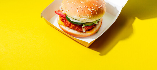 A delicious and juicy burger with a fish cutlet in a paper box on a yellow background. Stylish...