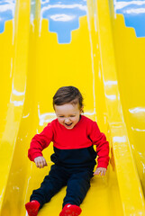 Happy, smiling handsome little boy, preschool child descends, slides down plastic slide at indoor...