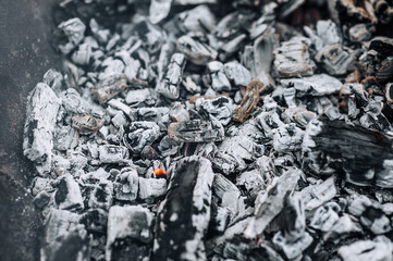 Close-up photo of smoldering gray coals, close-up burnt ash in a campfire, fire with smoke.
