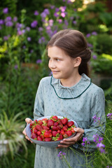 Cute girl in a vintage dress with a bowl of ripe strawberries in the garden