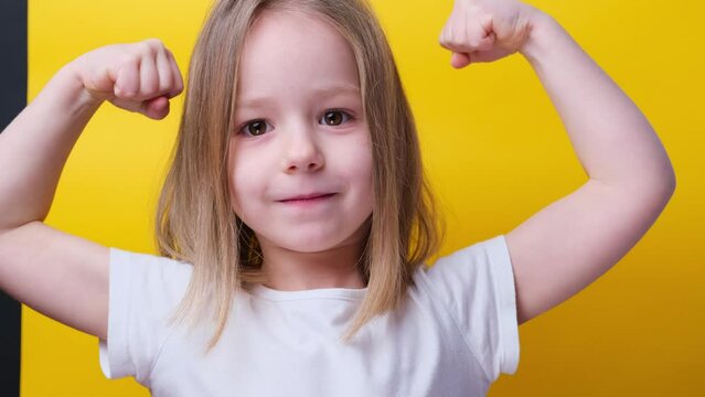Strong power preschool little girl flexing arm muscle smile posing yellow background looking on camera