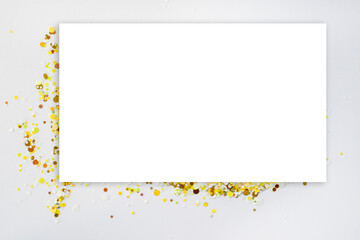 Blank white rectangular card on gold confetti. Space for inscription or design. Top view. Mock up.
