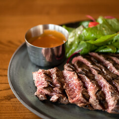 Juicy medium rare meat steak. Meat is cut into pieces and served on plate with sauce and lettuce leaves. Wooden table. Close-up. Soft focus. 