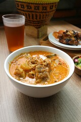 A bowl of beef curry with carrots served with a glass of tea on a wooden table