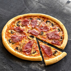 Pizza with ham and mushrooms. Round pizza with slice cut off. Italian Cuisine. Fast food. Dark gray background. Close-up. Copy space. Top view. 