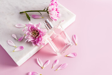 a beautiful transparent bottle with a cosmetic natural remedy, spray or perfume leaned on a marble white podium with petals and flower buds.