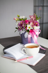 Notepad with a mug of tea and flowers. Day planning. Bouquet of alstroemerias, orchids, roses and white chrysanthemums.