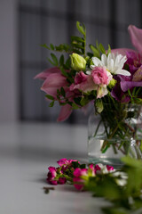 Flowers in a glass vase on a white table. Bouquet of alstroemeria, orchids, roses and white chrysanthemums.