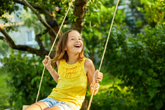 Happy barefoot laughing child girl swinging on a swing in sunset summer day