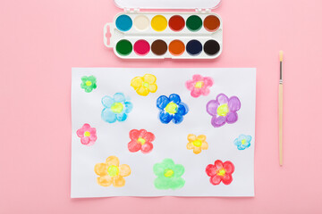 Colorful flower heads draw on white paper on light pink table background. Closeup. Pastel color. Top down view.