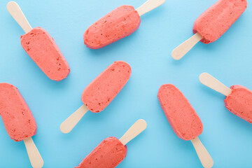 Red strawberry ice cream with sticks on light blue table background. Pastel color. Closeup. Cold...