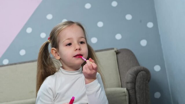 beautiful little girl child mirror makes a make-up pink lipstick imitates adults
