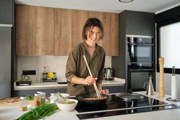 Smiling asian young man cooking chinese or taiwanese tomato scrambled eggs at kitchen.