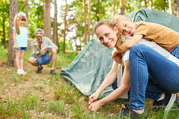 Fototapeta premium Woman piggybacking son setting up tent in forest