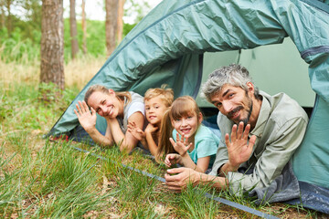 Happy family waving in tent camping in forest