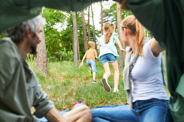 Parents sitting inside tent while children running in forest