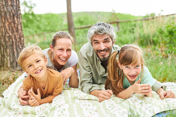 Fototapeta premium Smiling family lying on blanket in forest during vacation
