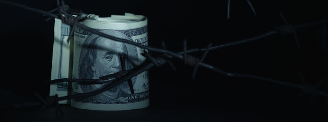 Close up barbed wire against US Dollar bill as symbol of economic warfare, sanctions and embargo busting. Selective focus. Horizontal image.