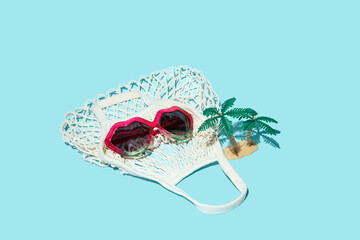 Creative summer holidays concept,  sunglasses, tropic palm tree and mash bag, pastel blue background. 