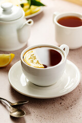 Drinking tea. White, ceramic cup with black tea and lemon slice. Neutral background.