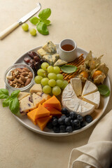 Cheese board, platter with assorted various cheeses, fruits, nuts and snacks. Warm background.