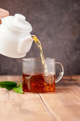 Pouring black tea in glass cup, wooden table. Hot beverage.