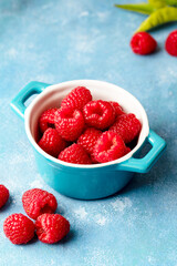 Fresh raspberry fruits in blue bowl, blue background