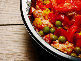 Ready made Spanish paella in a black plastic dish for microwave on a wooden table. Premium quality meal for take away or on the go. Food with rice and shrimp and chorizo.